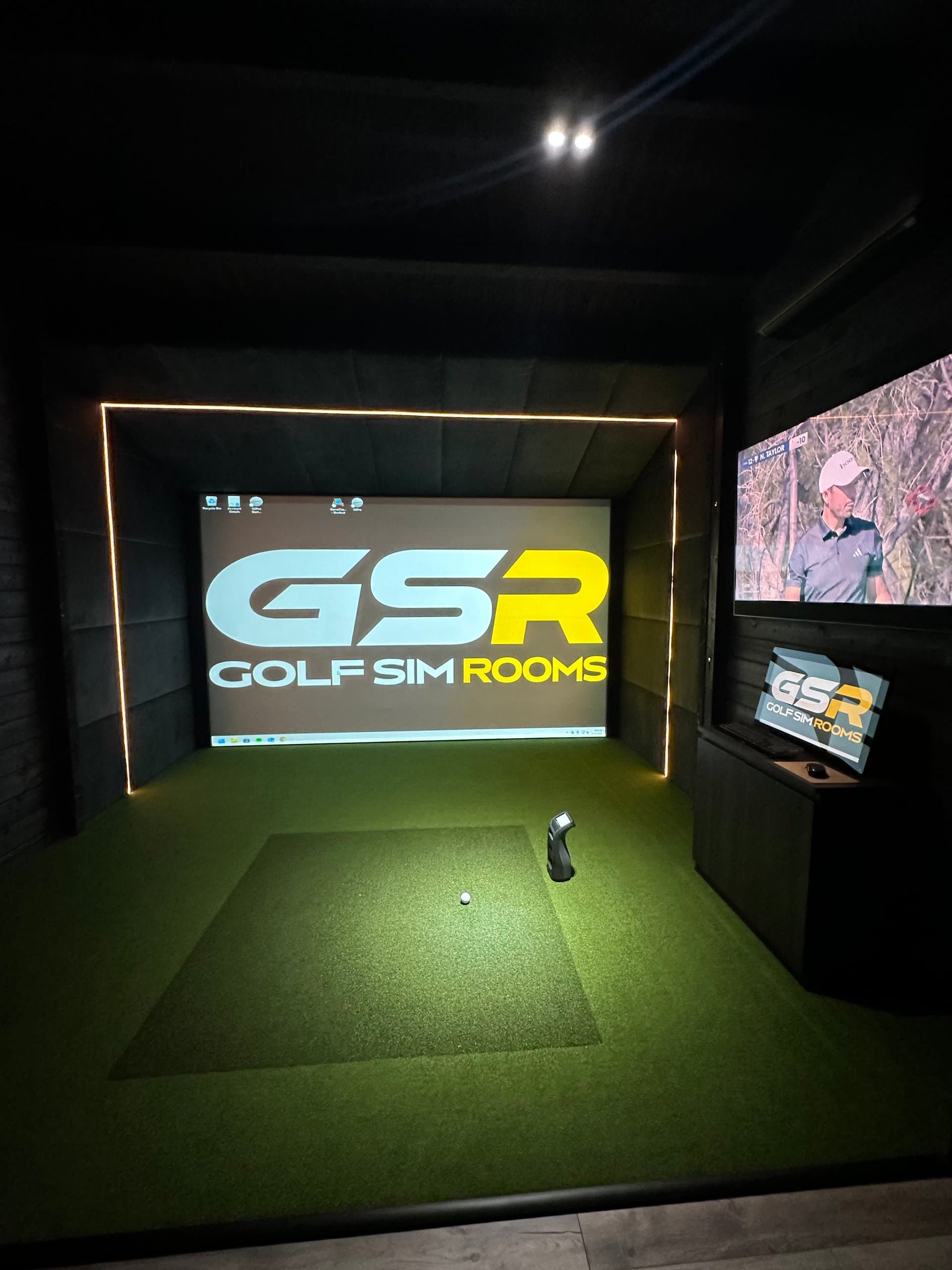 Simulator bay with the GSR logo on the screen inside an LED-edged frame and a TV on the side wall