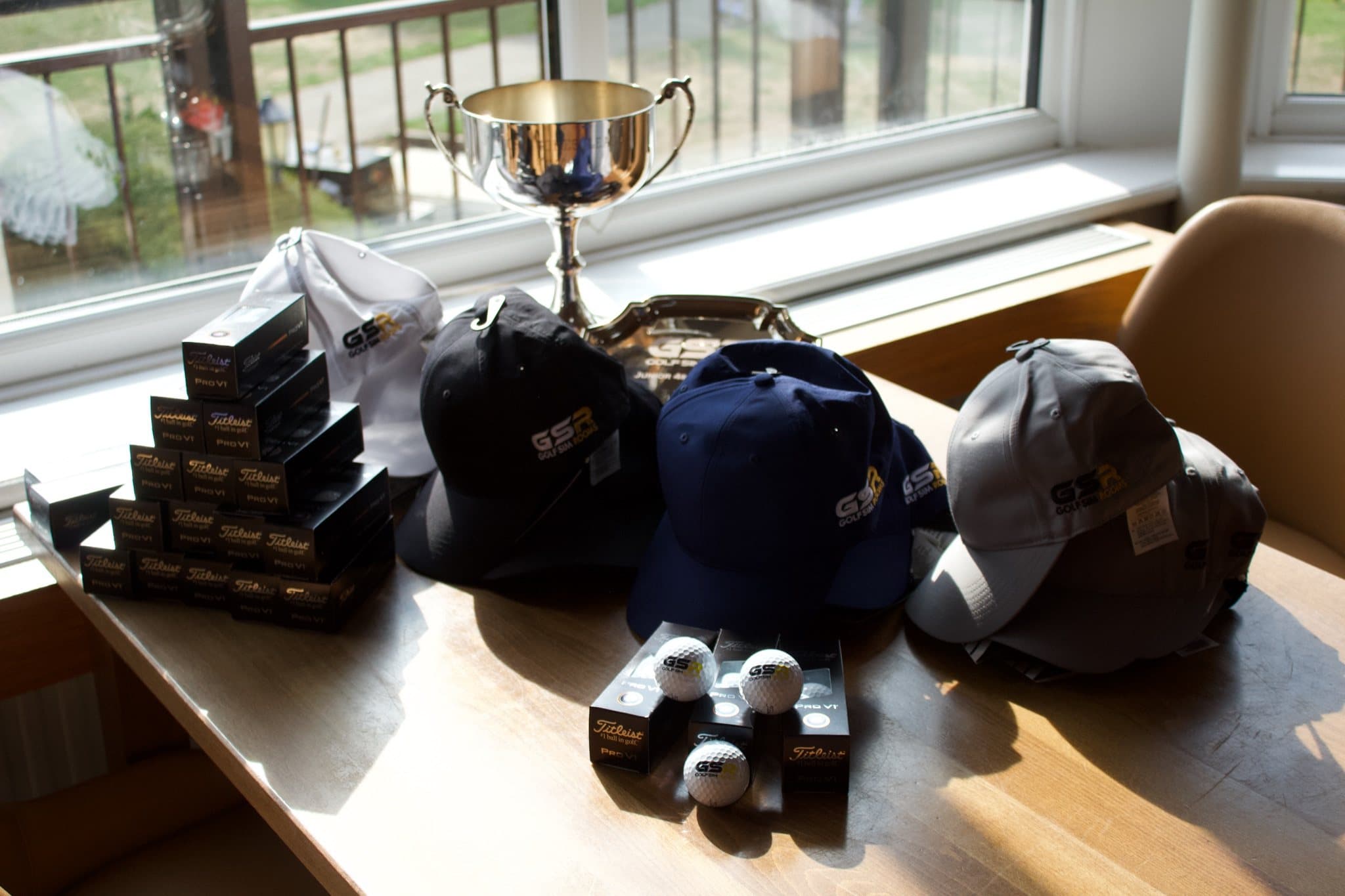 The cup, the engraved plate, GSR caps and boxes of golf balls laid out on a clubhouse table