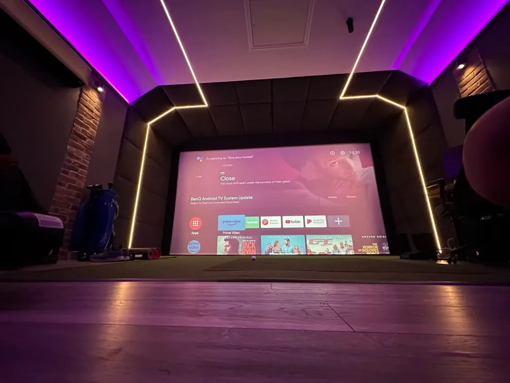 Simulator screen showing a TV menu, framed by LED lines under purple ceiling lighting, golf bags to the left