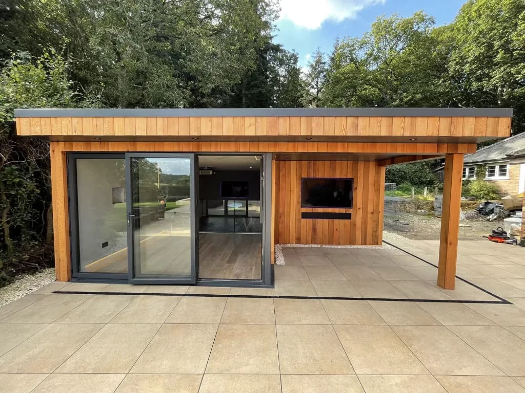Timber-clad garden building with sliding glass doors and a covered terrace, seen from the patio