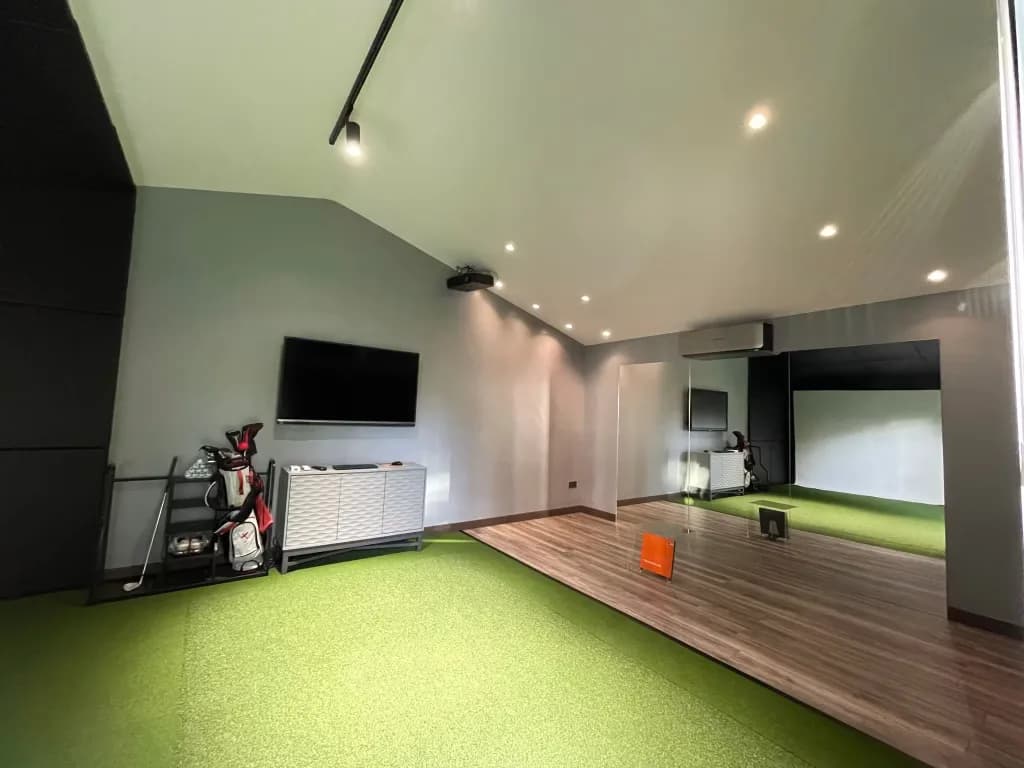 Long room with a turf runway, a TV and golf bags on the side wall and the simulator bay at the end