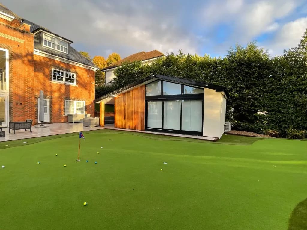 Wide view of a putting green in front of a glazed garden room, with the house to the left