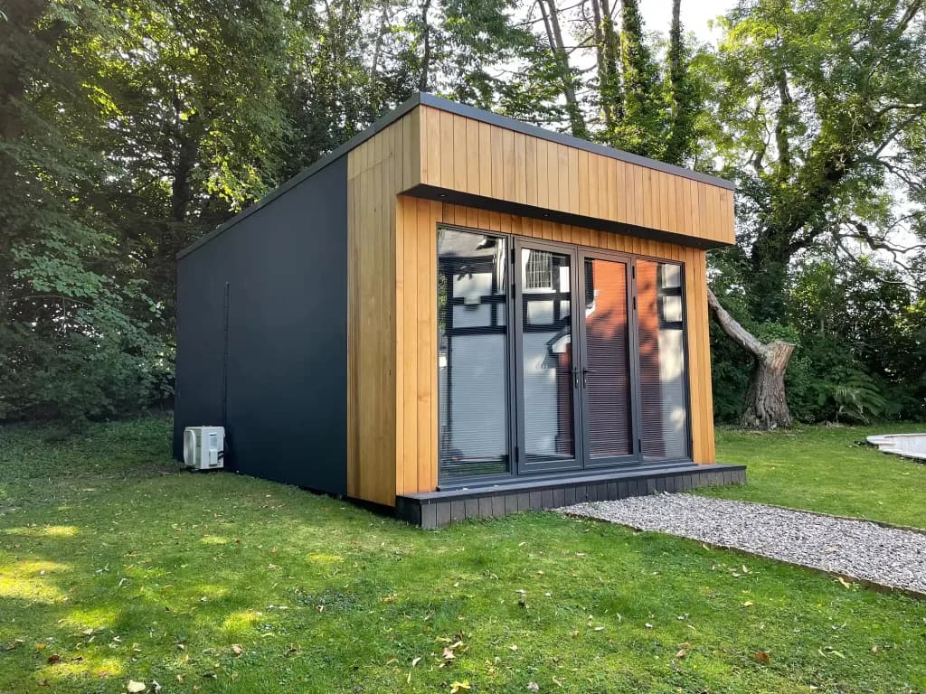 Garden room clad in timber and dark panels, with glass doors, on a lawn