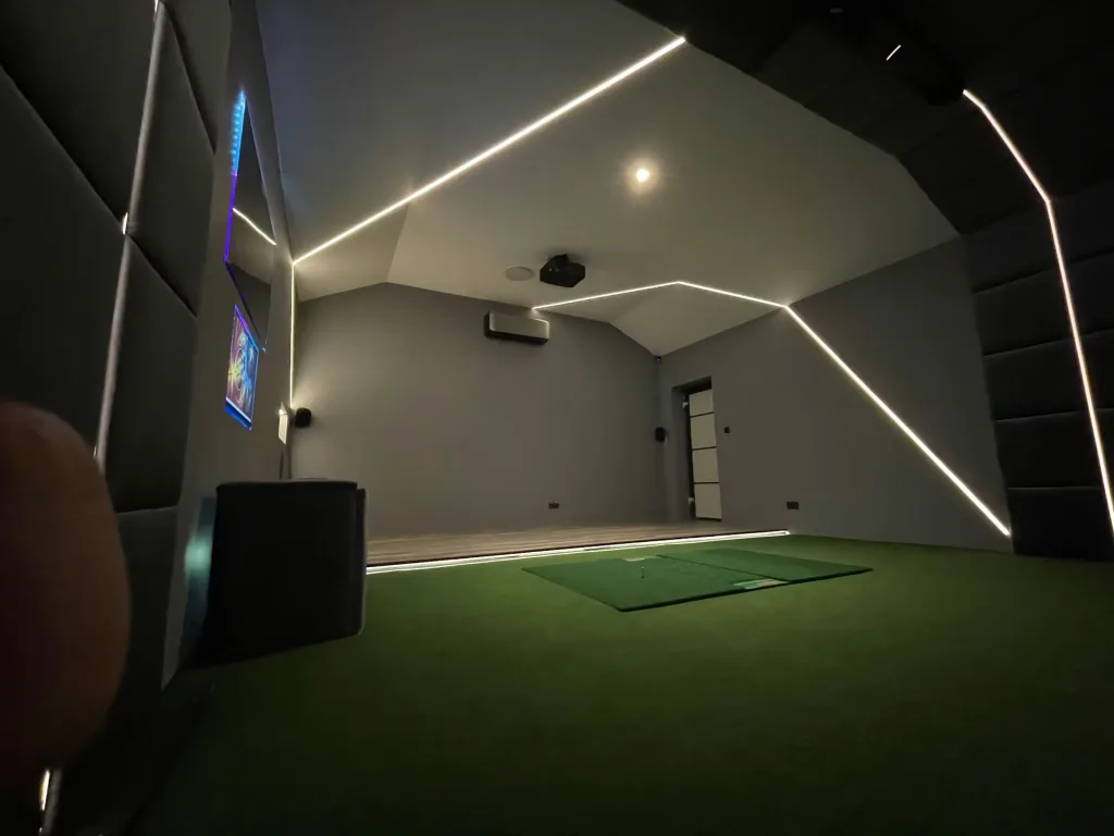 Inside a converted garage looking away from the screen: turf, LED lines on the ceiling and a door at the far end