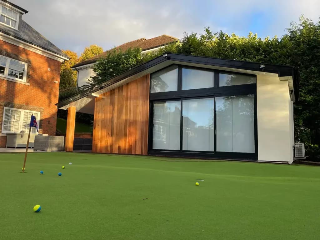 Garden room with a glazed gable end and timber cladding, behind a putting green with balls and a flag