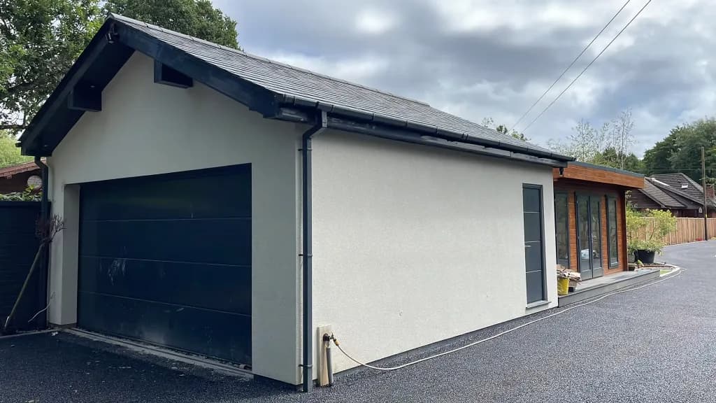 Rendered detached garage with a dark up-and-over door and a slate roof