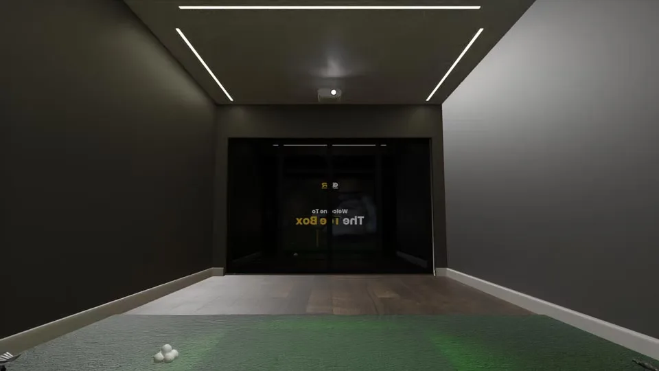 The Tee Box's glass doors seen from the hitting mat, under strip lights in the ceiling