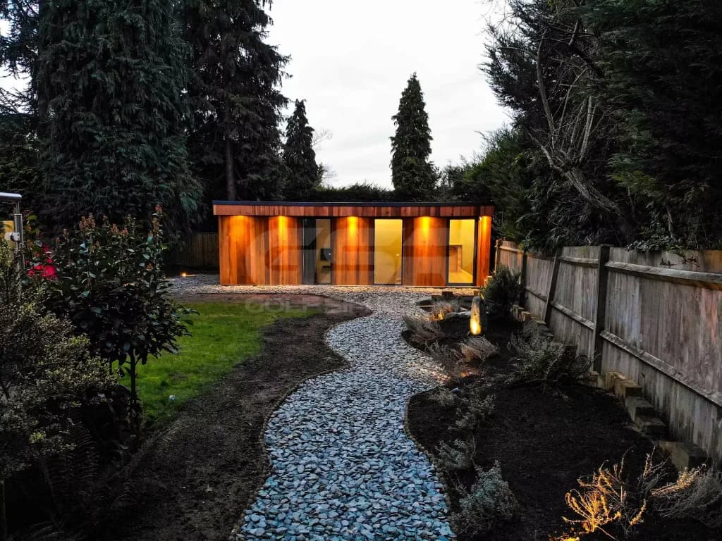 Gravel path winding through the garden to the cedar-clad garden room at dusk