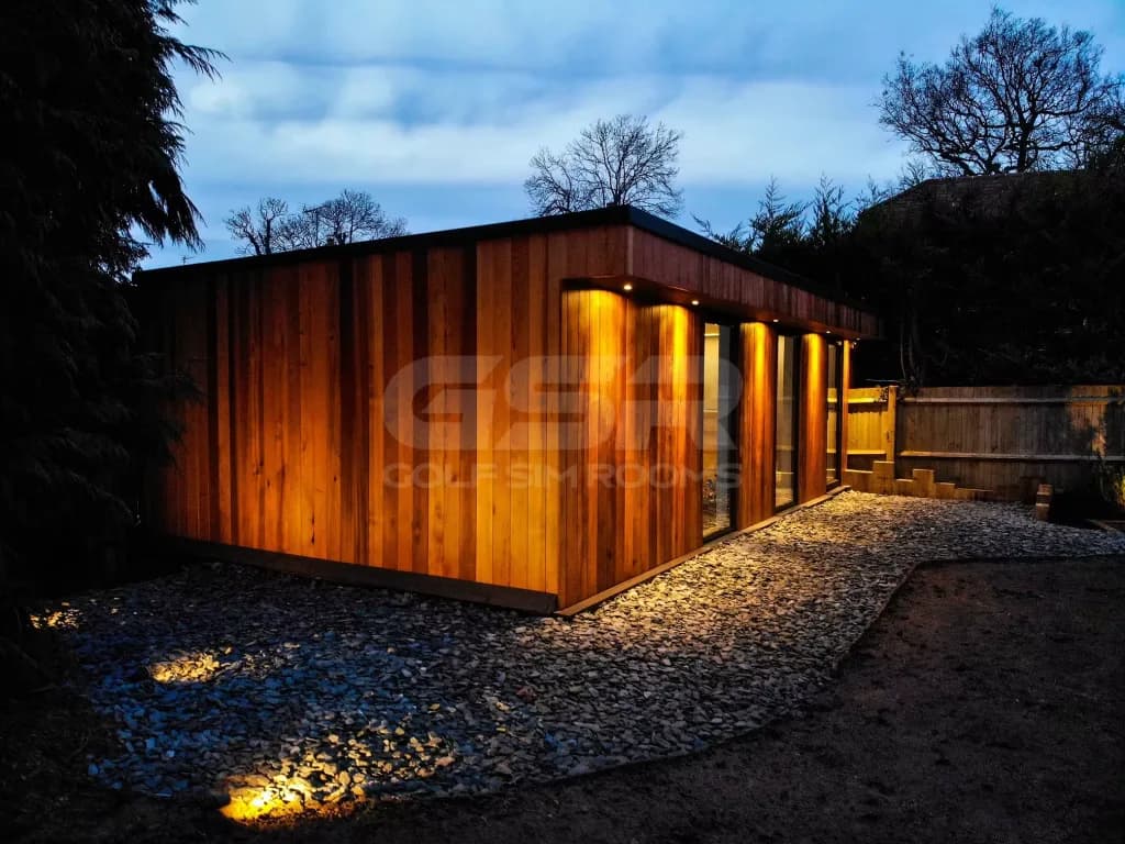 Side of the cedar-clad garden room at dusk, with ground lights along the gravel