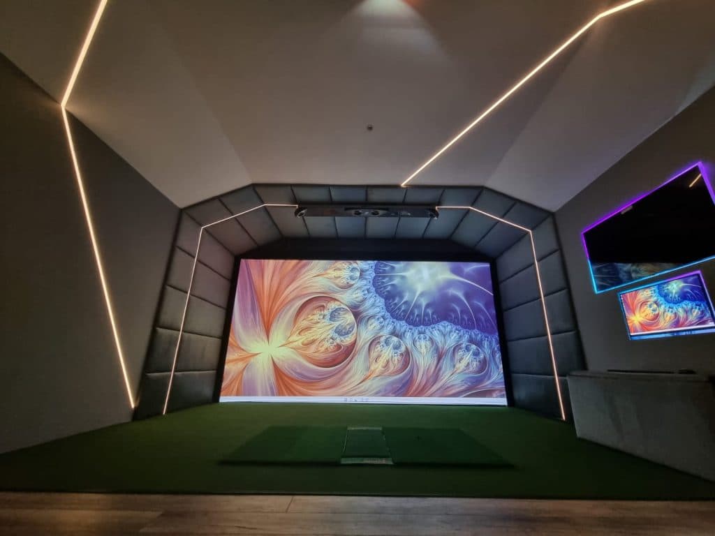 Simulator bay with white LED lines running across the ceiling and walls, a colourful image on the screen and two wall TVs