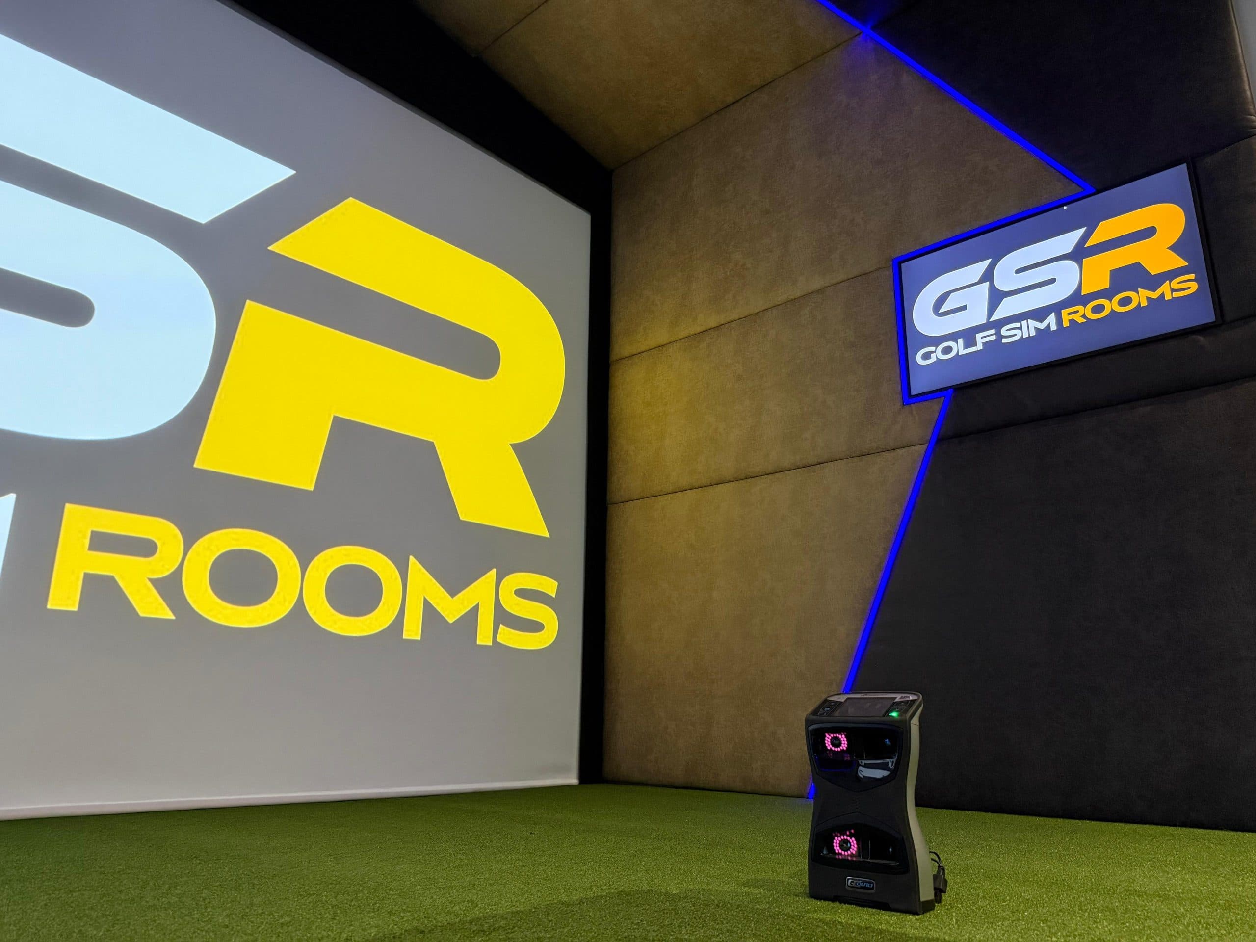 Simulator screen showing the GSR logo, a GSR sign on the padded side wall and a launch monitor on the turf