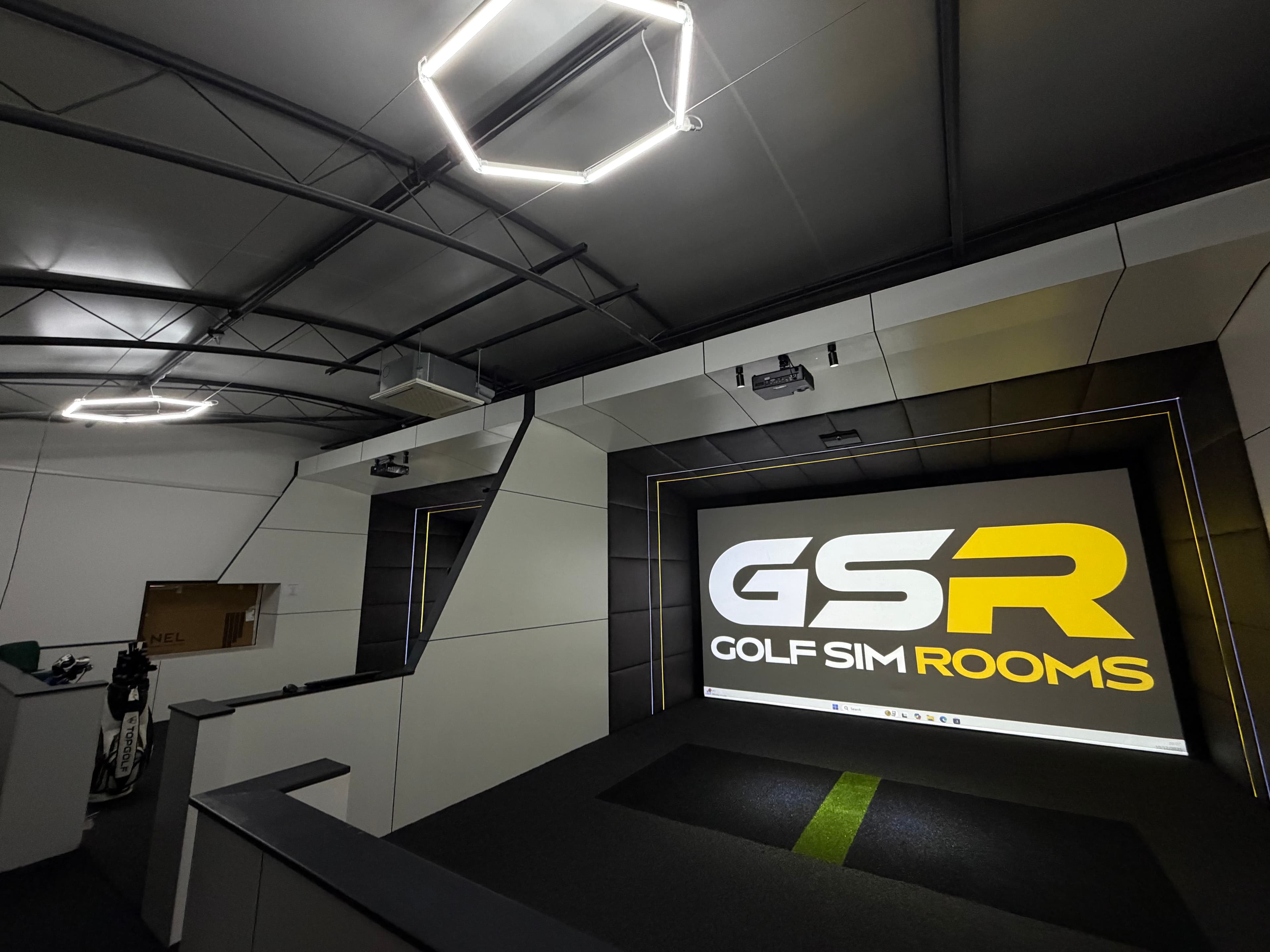 Simulator bay showing the Golf Sim Rooms logo under hexagonal ceiling lights