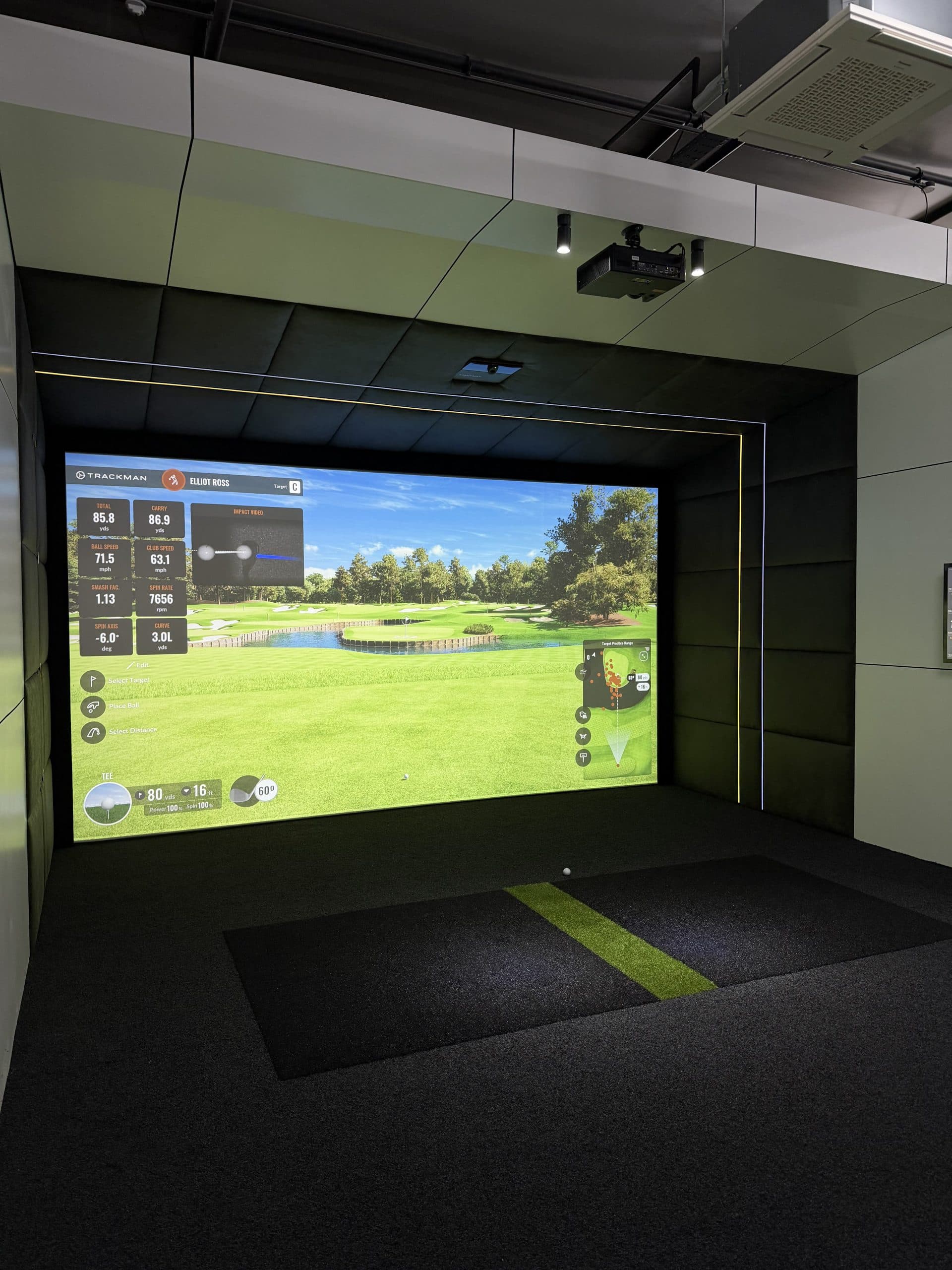 Simulator bay with a course on the screen and a green stripe across the mat