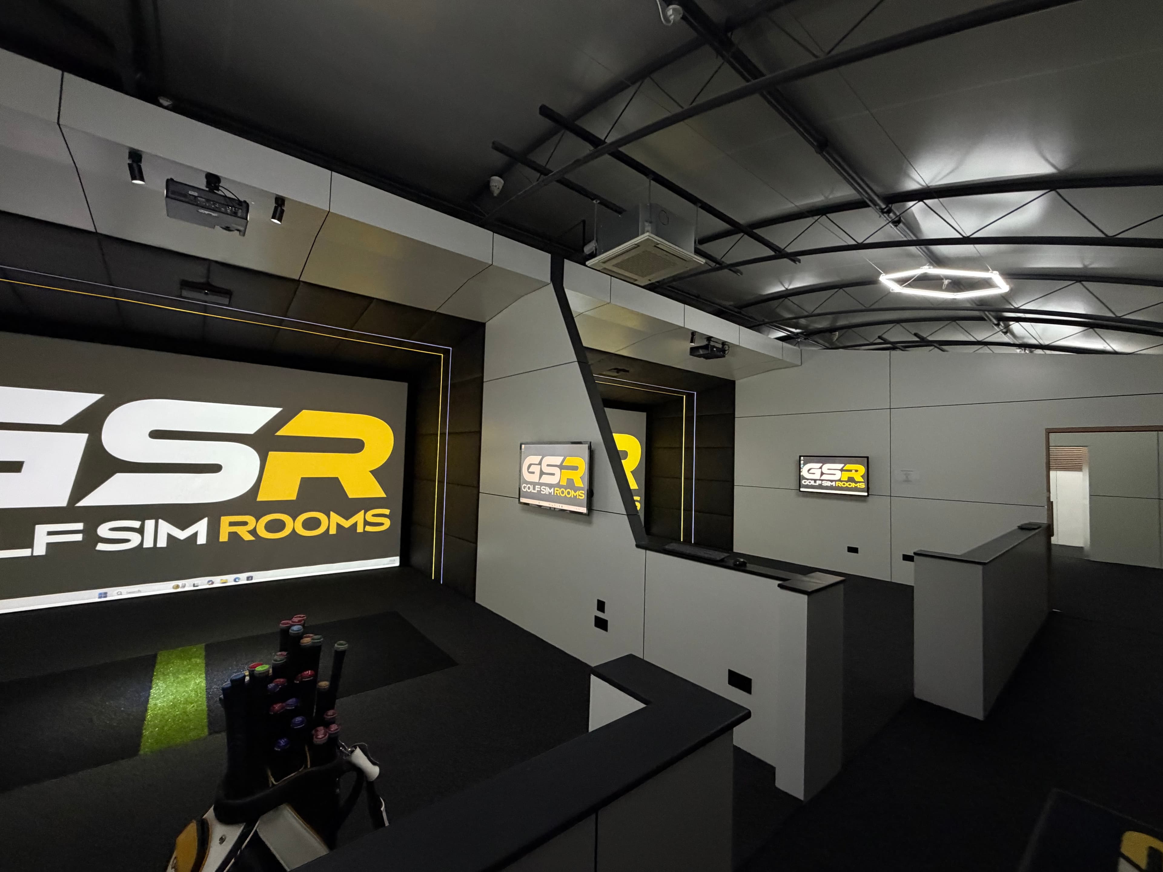 Simulator bays with the Golf Sim Rooms logo on screen, partitions between them and a golf bag in the foreground