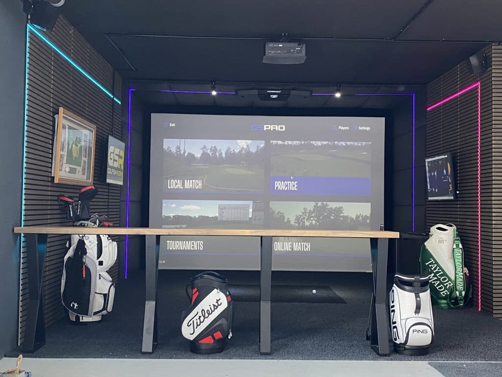 Golf bags lined up under a high table in front of the simulator screen, with multicoloured LED edging