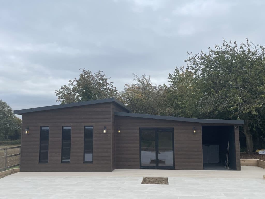 Brown-clad garden room with tall narrow windows and glass doors on a paved patio