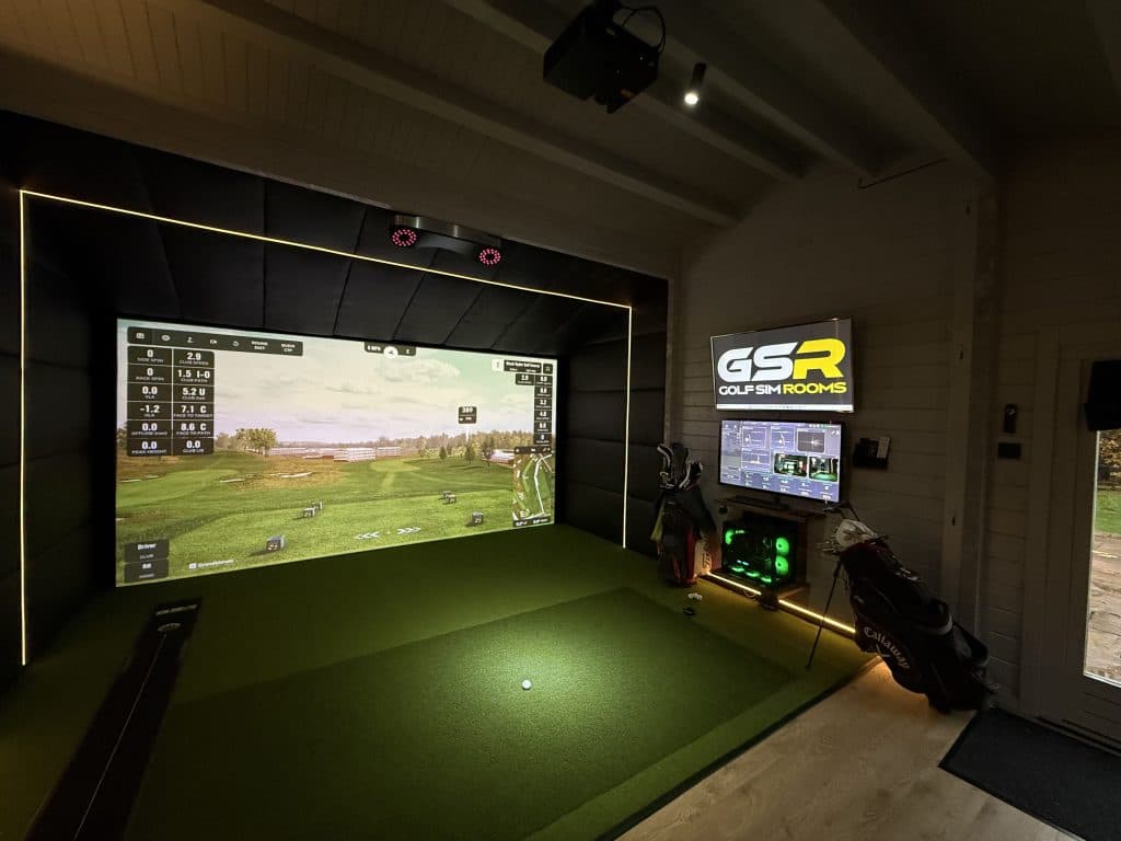 Log cabin simulator with shot data on the screen, a GSR sign above a monitor and golf bags beside the bay
