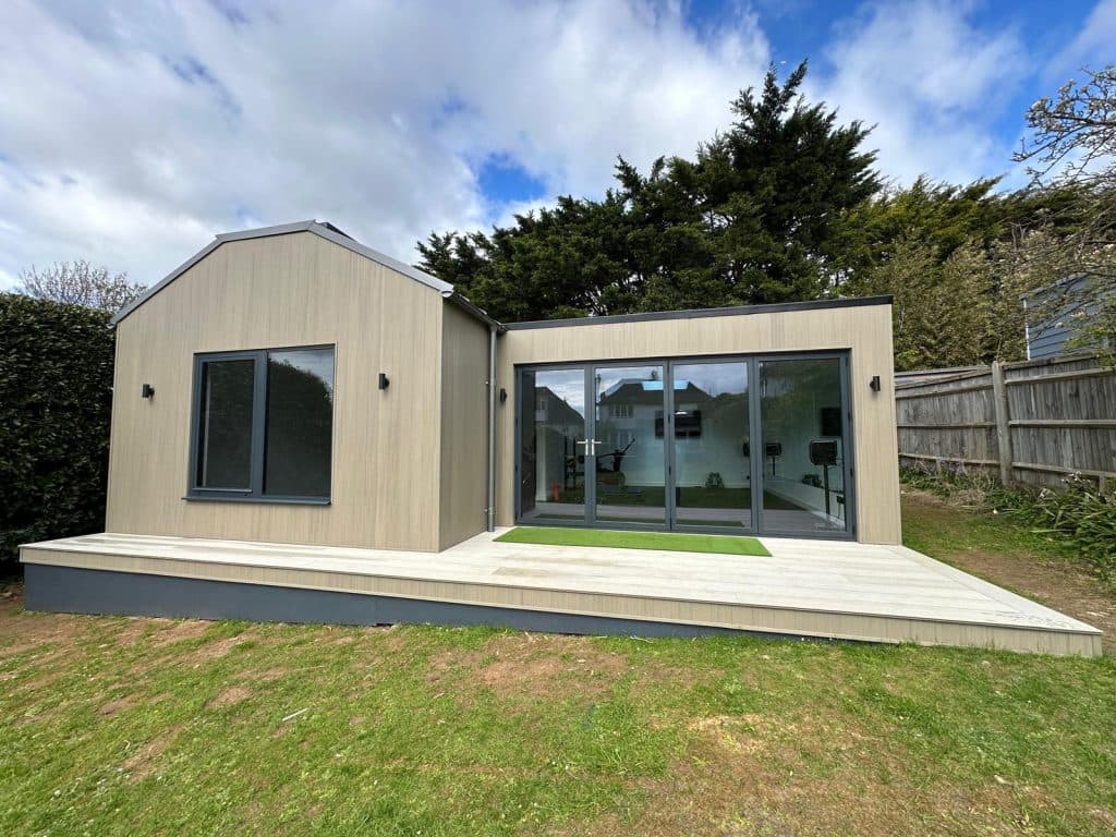 Front of the light-clad garden room, with wide glass doors and a strip of turf on the decking