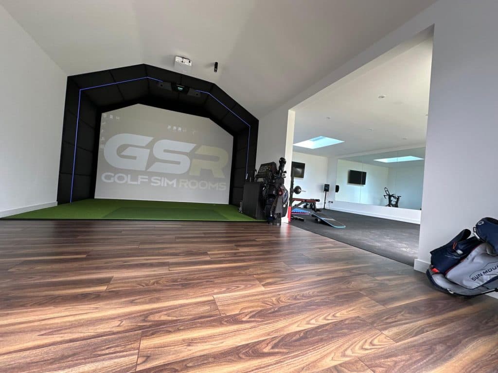 Garden room on a wooden floor, the Golf Sim Rooms logo on the screen at one end and gym equipment beyond