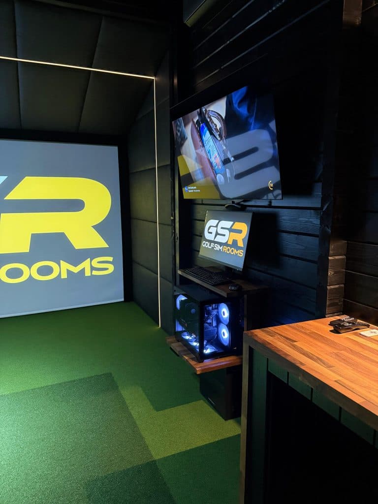 Inside the cabin: the Golf Sim Rooms logo on the screen, a TV and gaming PC on the dark wall, and a wooden counter
