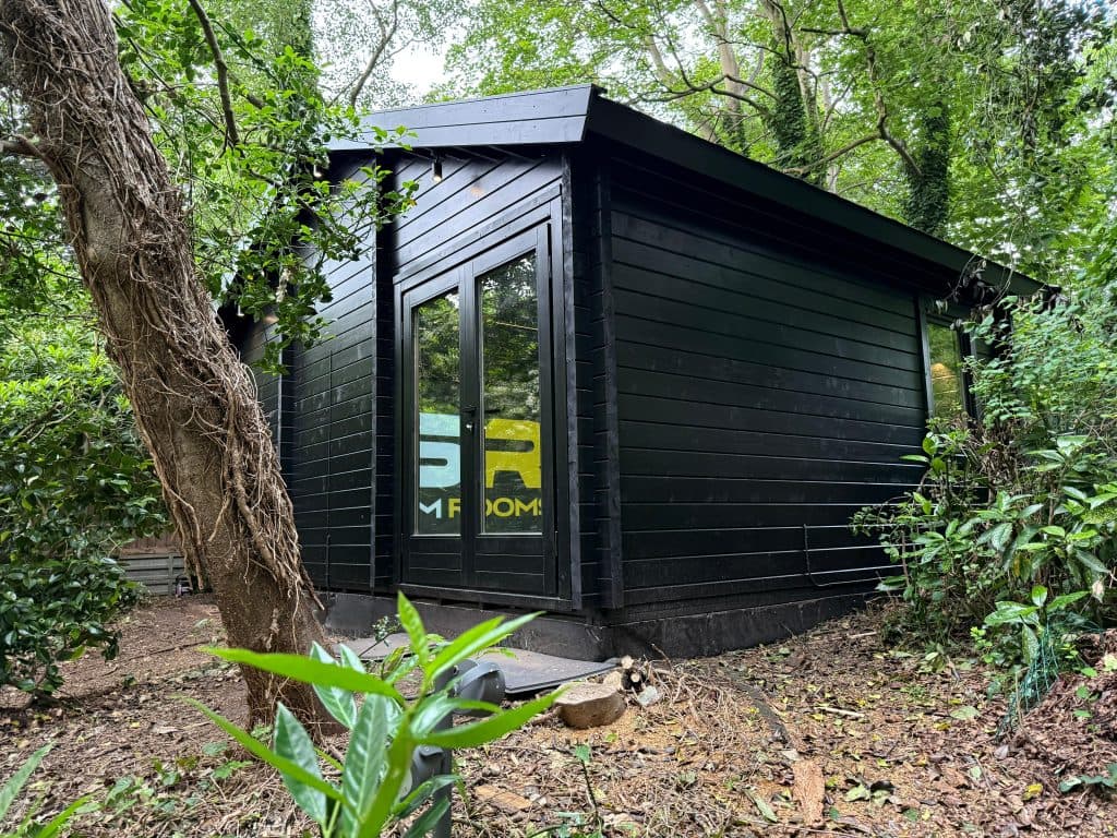 Black-clad garden room among trees, with glass doors showing the GSR logo inside