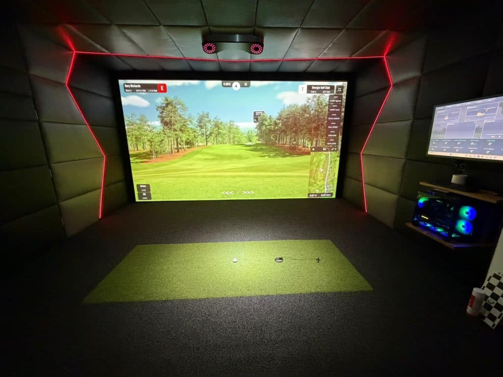 The simulator room: a course on the screen, red LED edging, padded walls and a hitting mat on dark flooring