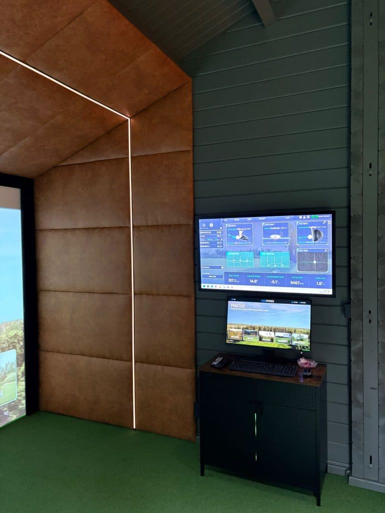 Cabin simulator with a tan padded wall, LED edging and two monitors on a cabinet