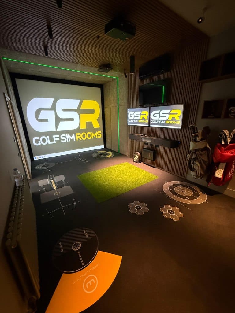 Narrow simulator room with the GSR logo on the screen, two small GSR screens on the wall and a printed floor