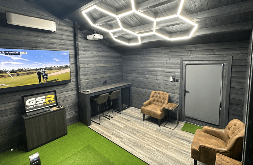 Simulator room with hexagonal ceiling lights, a TV, two armchairs and a counter by the door