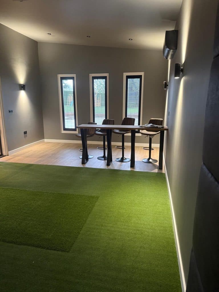 Room with turf flooring, three tall windows and a high table with stools